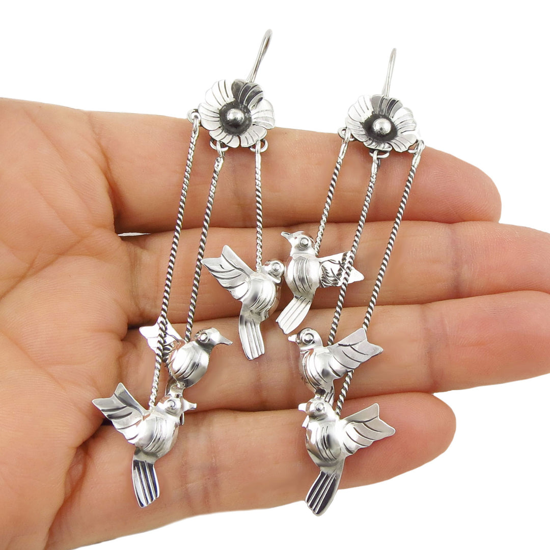 Mexican sterling 925 silver dangling lovebird chandelier earrings held in a hand against a white background