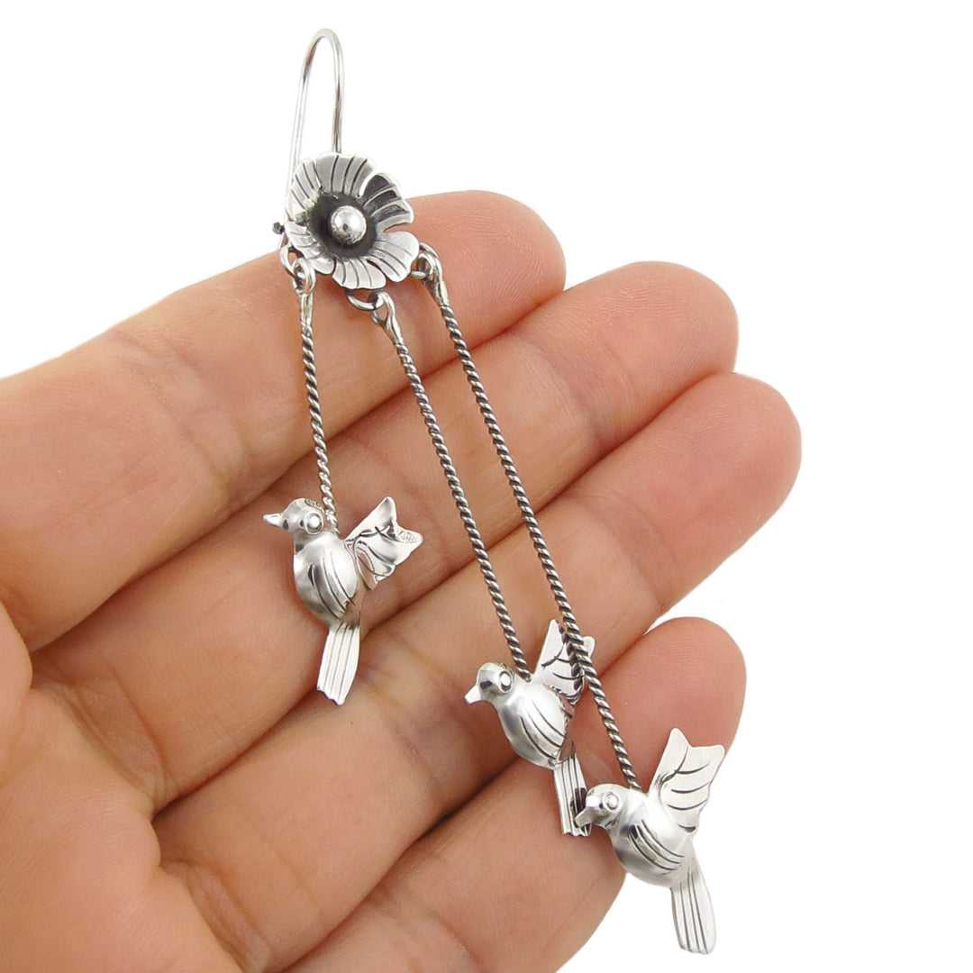Mexican sterling 925 silver lovebird dove dangling earrings held between fingers on a white background
