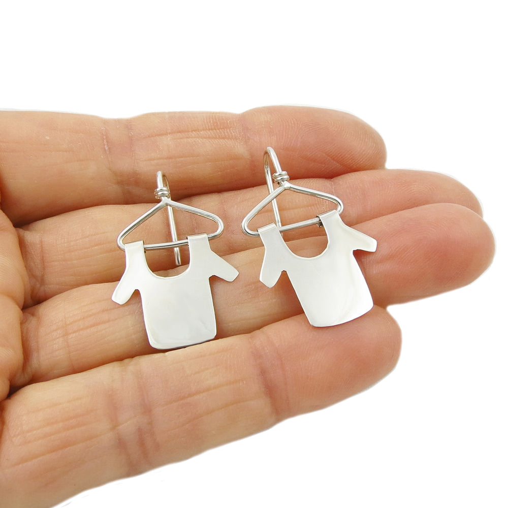 A pair of silver earrings designed in the shape of hangers with dangling tops and a polished finish, held in a person's hand.