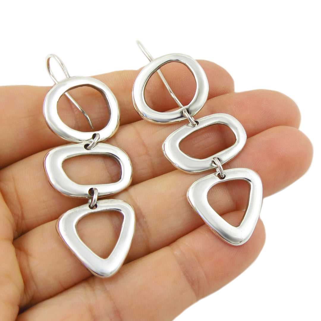 Silver earrings with geometric design held in a hand on a white background