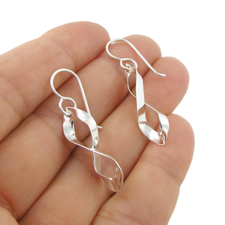 A pair of figure of eight earrings handmade from solid 925 silver held in a person's hand