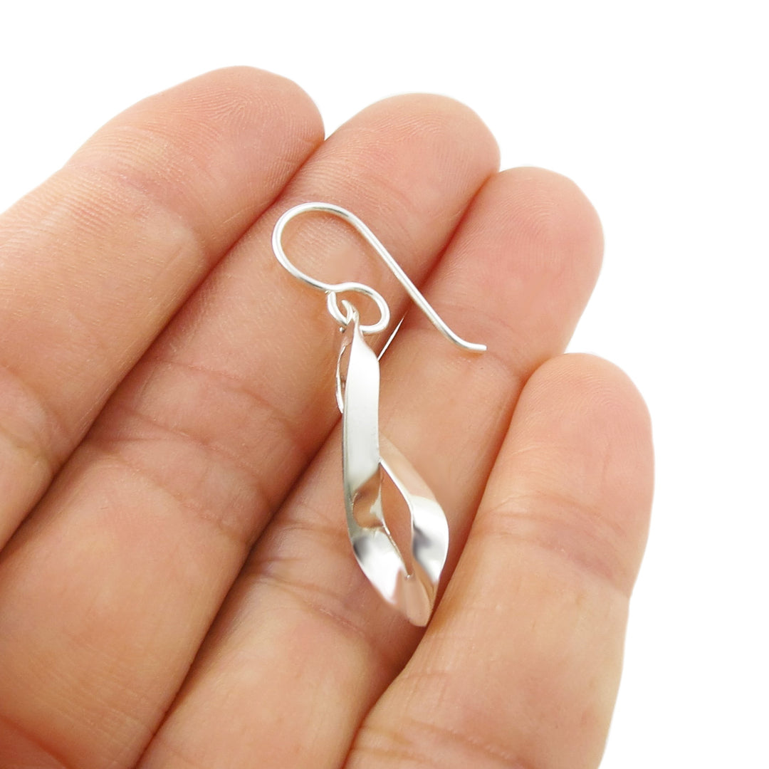 A single solid 925 silver figure of eight earring held in a person's hand on a white background. 