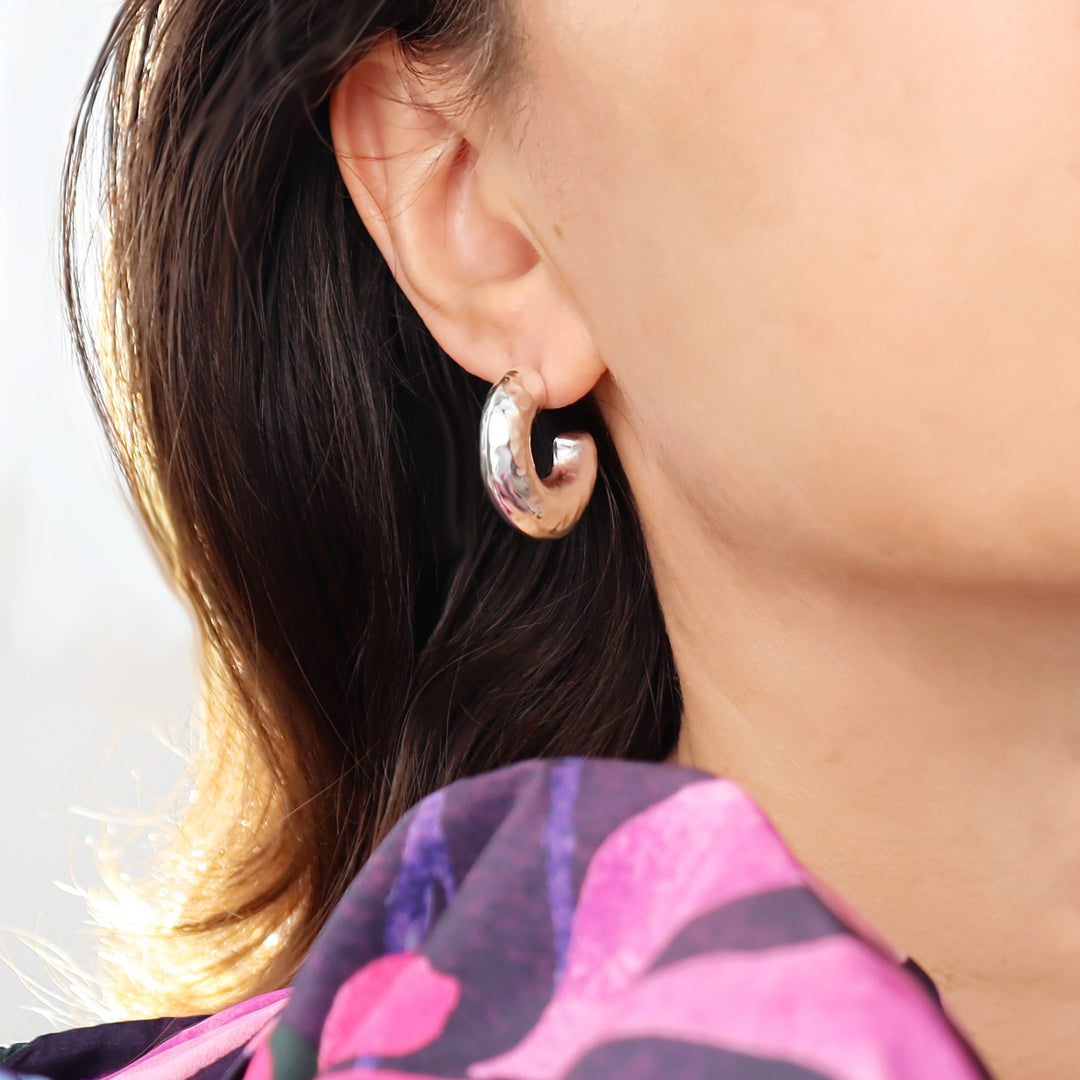 Close-up of a person wearing a silver puffed hoop earring with a blurred background