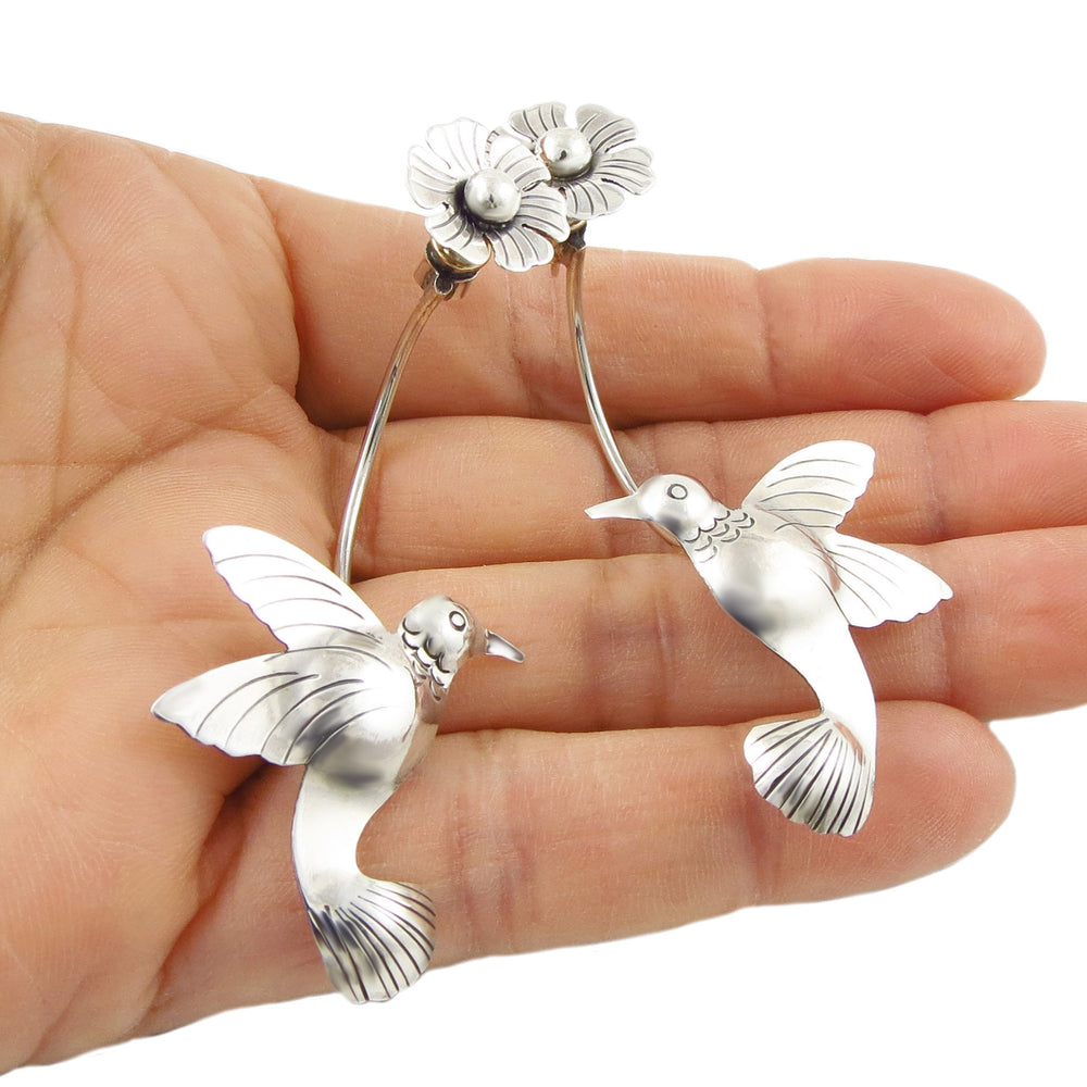 Large Mexican 925 sterling silver hummingbird and flower earrings held in a woman's hand against a white background