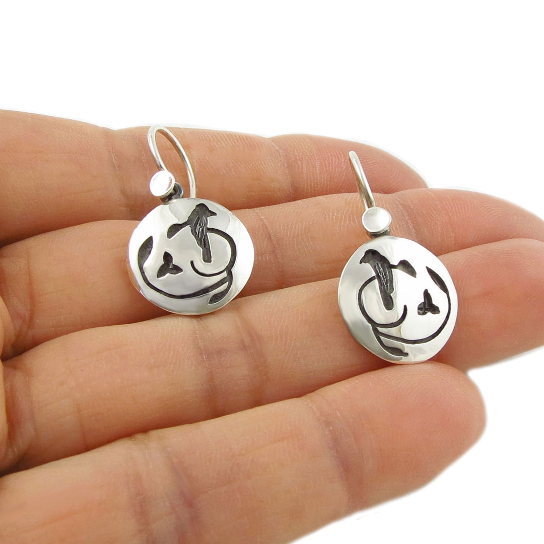 Artisan 925 Silver earrings with circular designs featuring nightingale birds held between fingers on a white background