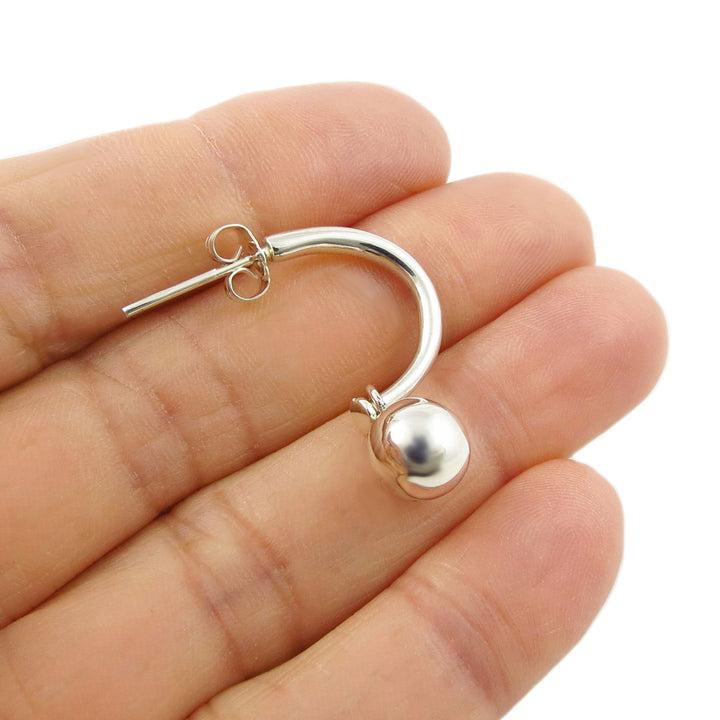 925 silver half hoop earring with a ball bead charm held between fingers on a white background