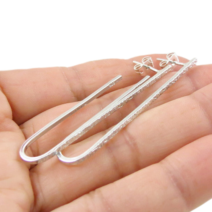 A pair of handmade unique 925 sterling silver long oval drop earrings with a battered finish on the front held in a person's hand. 