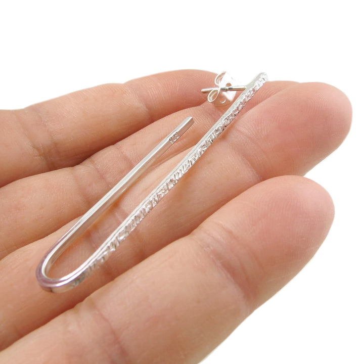 A 925 sterling silver handmade long oval drop earring with a post and butterfly fastener held between fingers on a white background