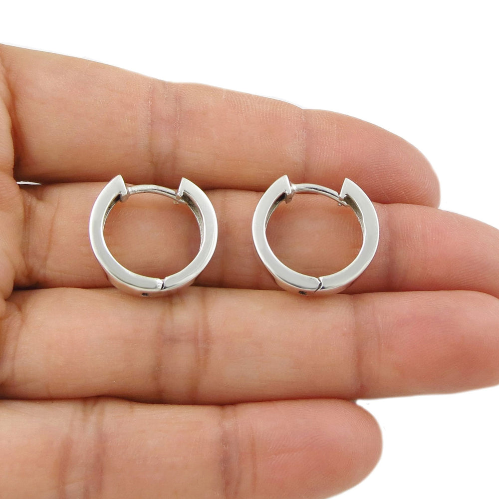 A pair of large chubby tunnel huggie circle hoop earrings for women held in a person's hand