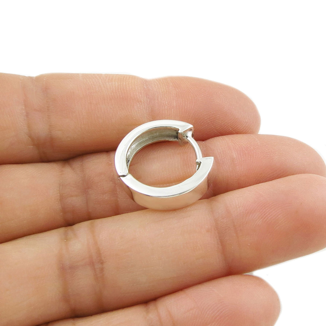 Women's sterling 925 silver huggie hoop earring held between fingers on a white background