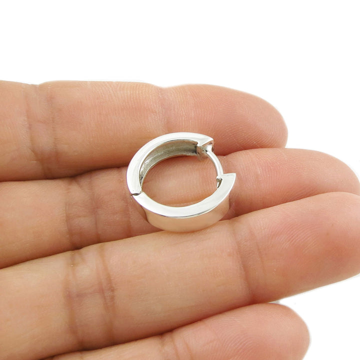 Women's sterling 925 silver huggie hoop earring held between fingers on a white background