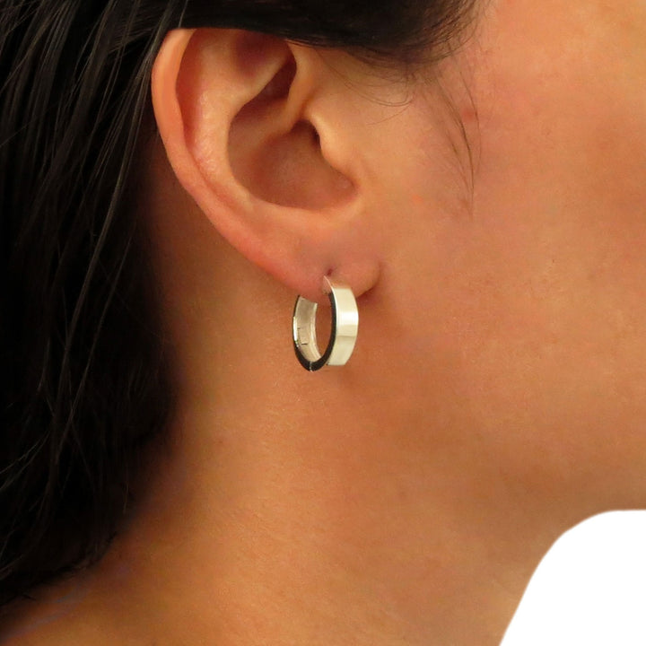 A large sterling 925 silver huggie hoop earring worn by a woman with dark hair