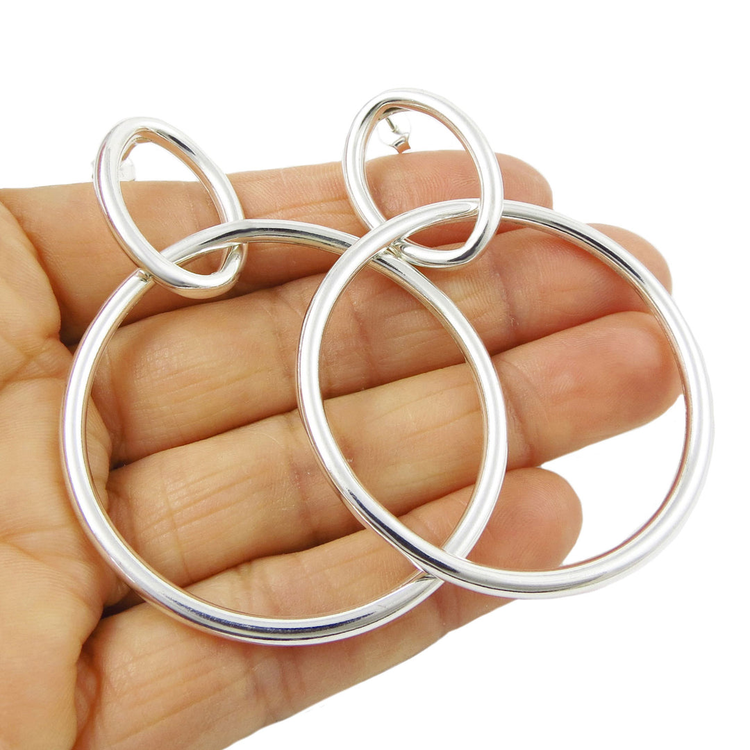 Large sterling silver double hoop earrings held in a woman's hand against a white background