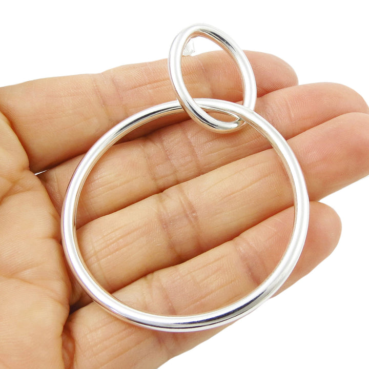 A single large sterling 925 silver tube hoop earring for women with a unique double circle design held in a hand against a white background