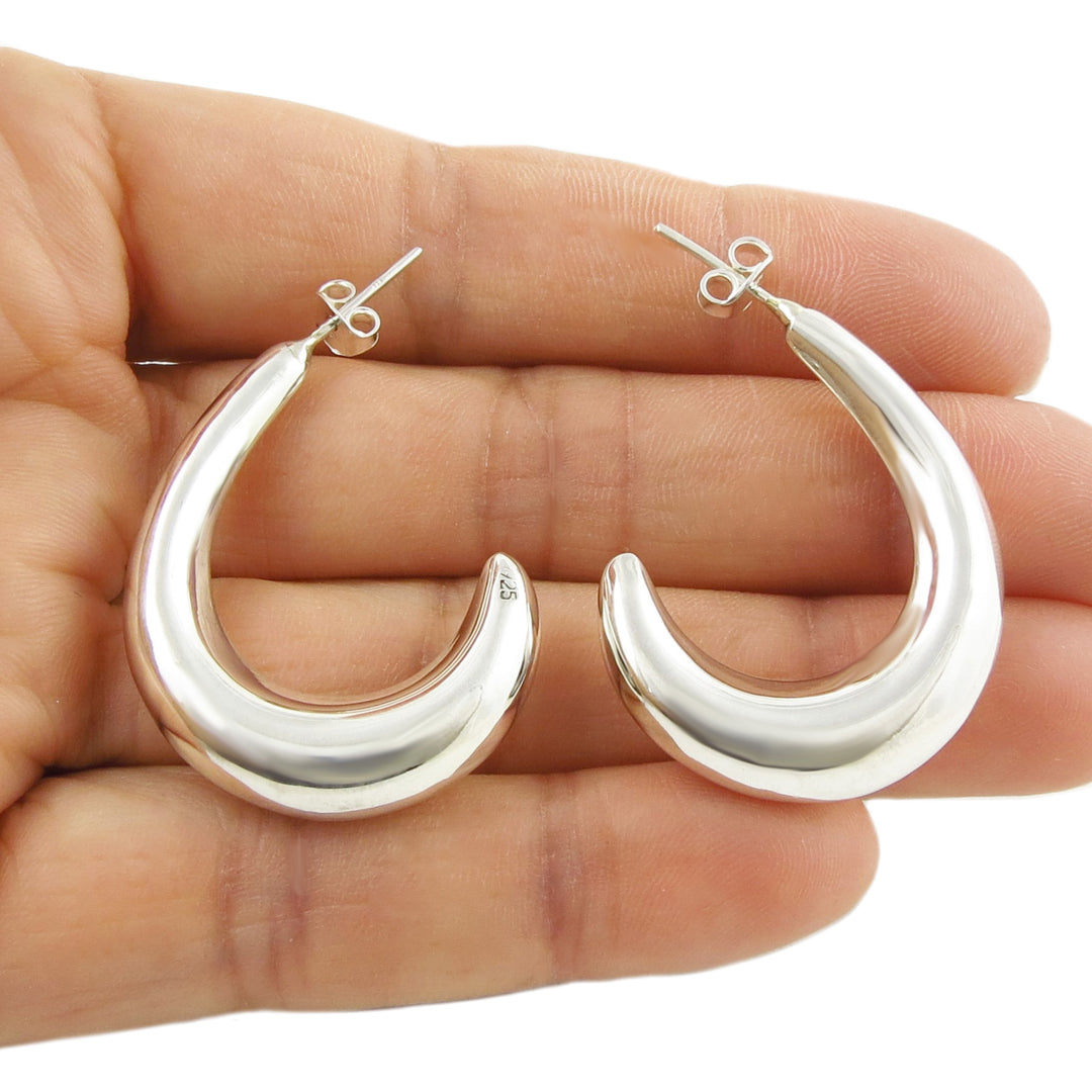 Large sculpted Mexican handmade 925 sterling silver hoop earrings held in a hand on a white background