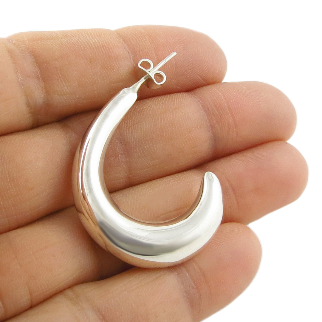 Mexican 925 sterling silver crescent moon half hoop earring held between a woman's fingers on a white background