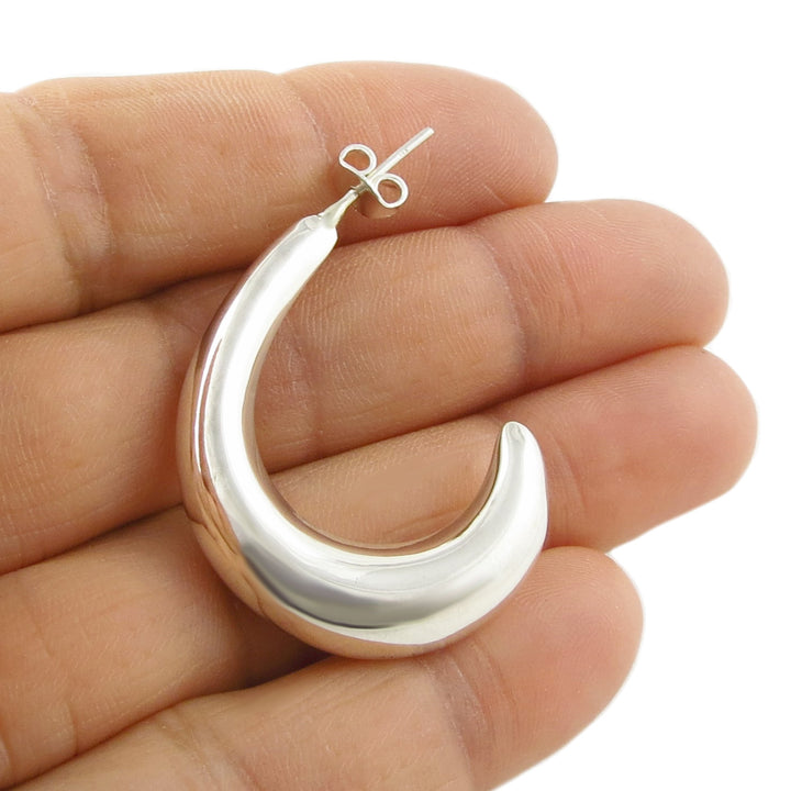 Mexican 925 sterling silver crescent moon half hoop earring held between a woman's fingers on a white background