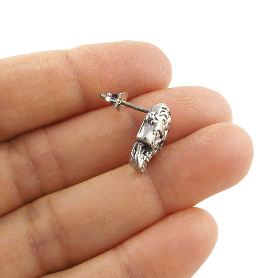A single Mexican day of the dead skull stud earring held between fingers on a white background