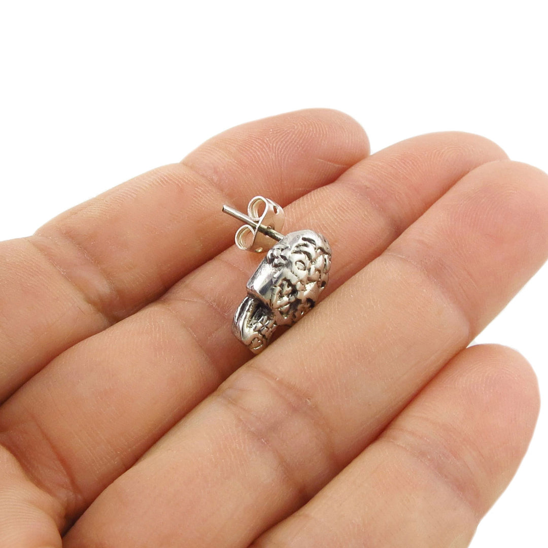 A single 925 Silver skull tud earring for women held between fingers on a white background