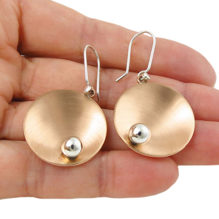 Brushed copper and 925 sterling silver handmade circle disc earrings held in a hand against a white background