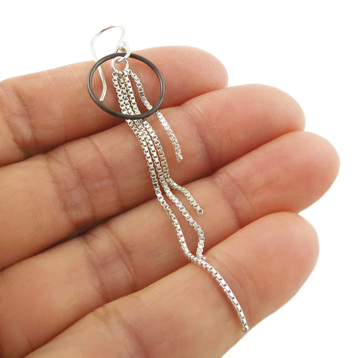 Sterling silver chain fringe earring held between fingers on a white background