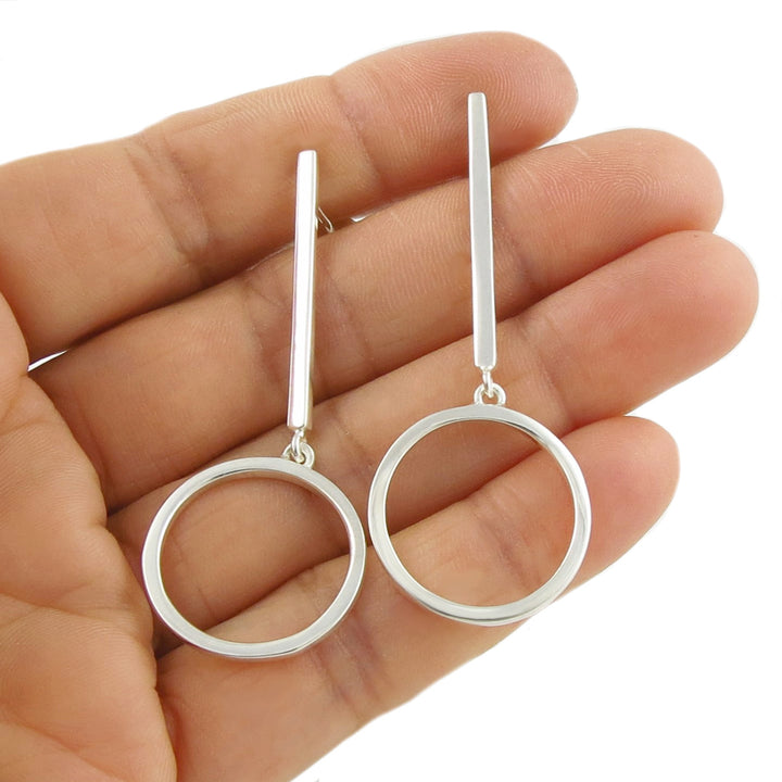 Long 925 sterling silver circle and stick drop earrings held in a woman's hand against a white background