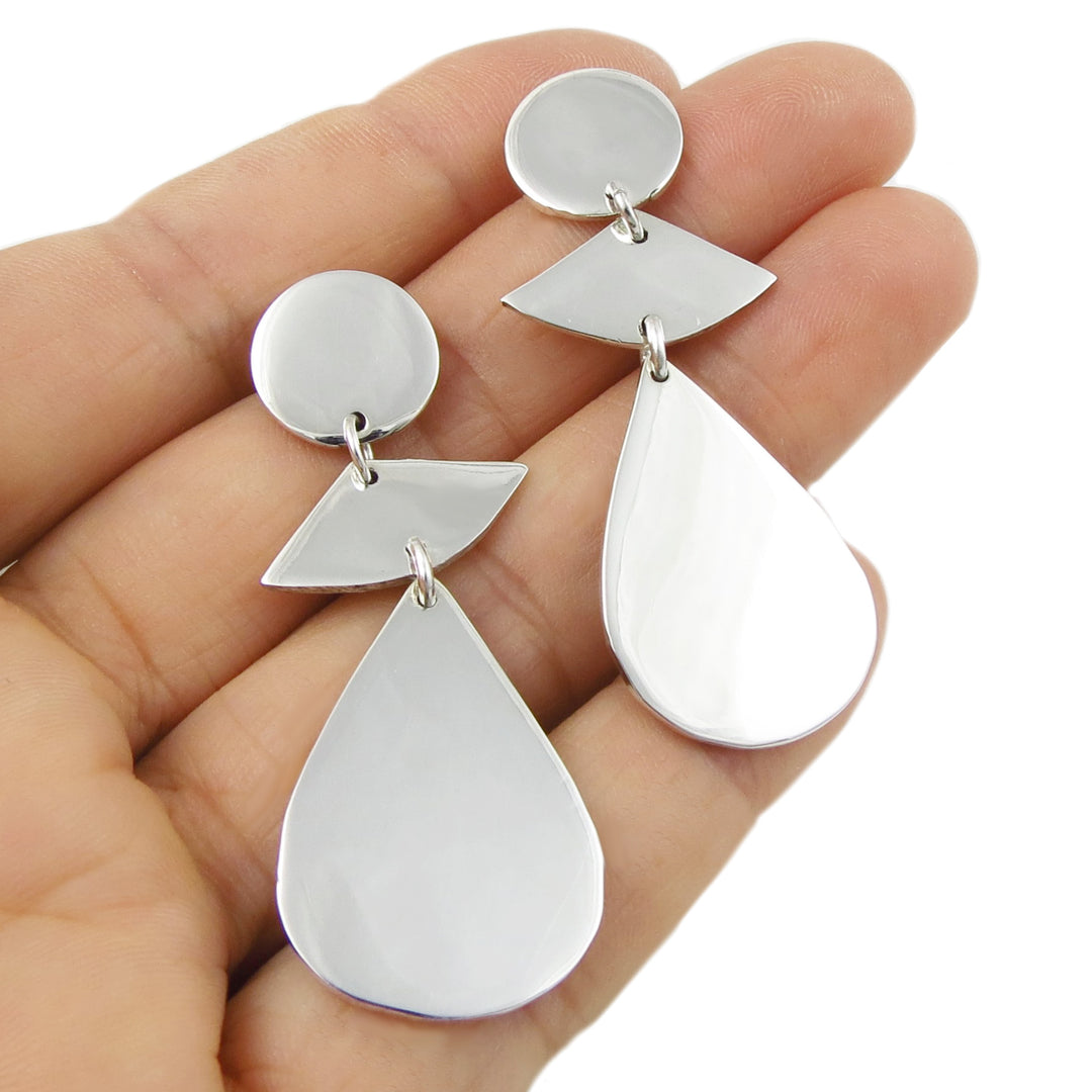 Long silver earrings held in a hand against a white background