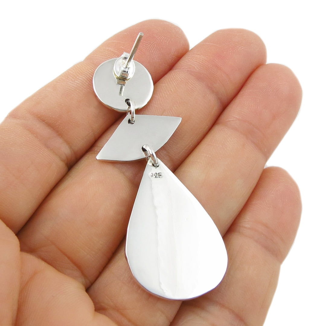 The reverse of a silver earrings held in a hand against a white background