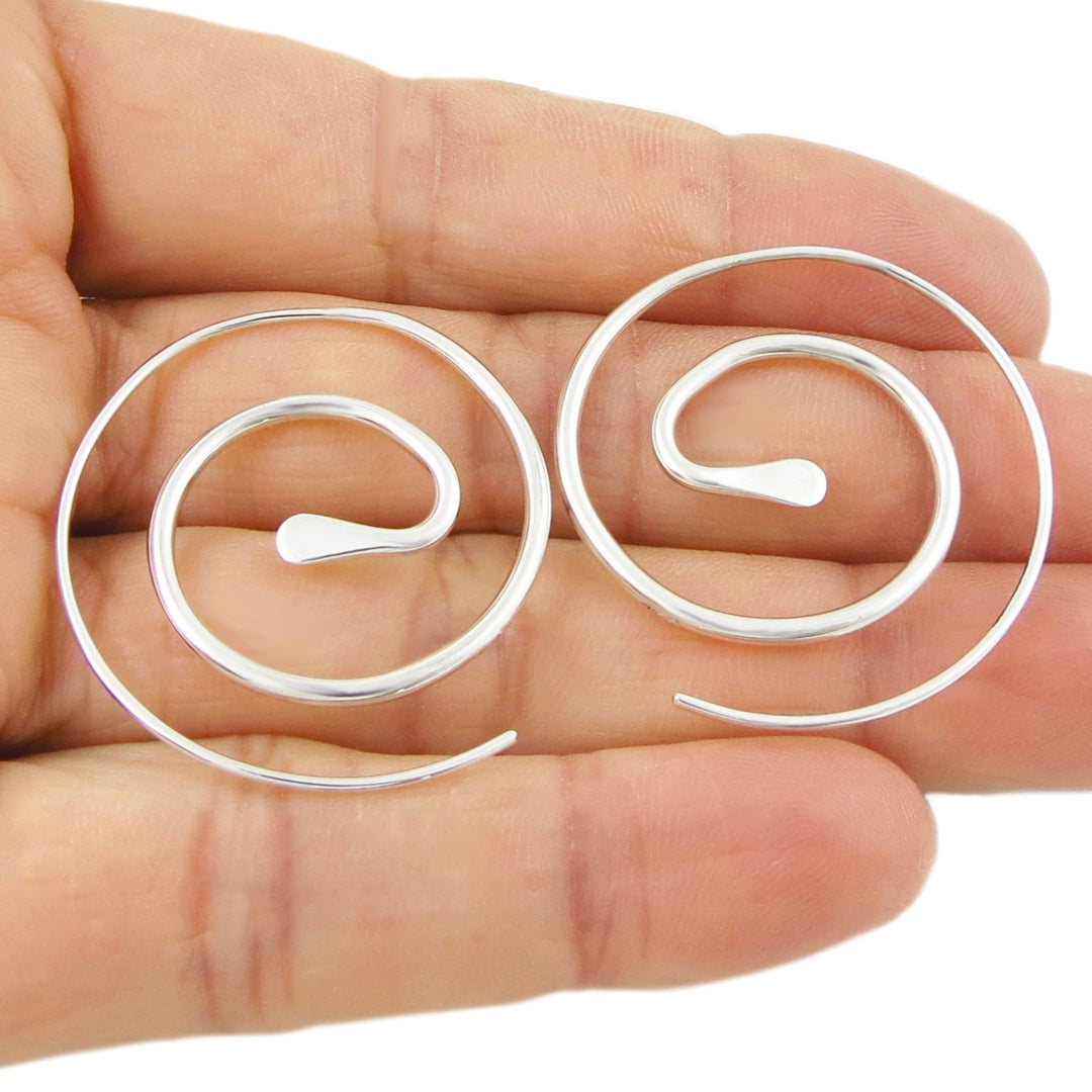 Large solid 925 sterling silver polished threader earrings in the shape of spirals held in a person's hand