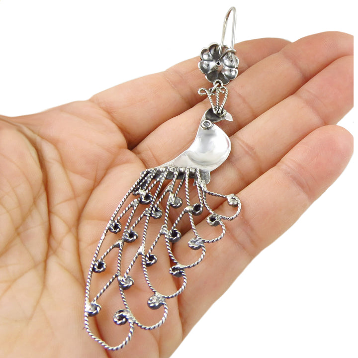 The reverse of a large 925 sterling silver chandelier earring in the shape of a peacock bird held in a person's hand.