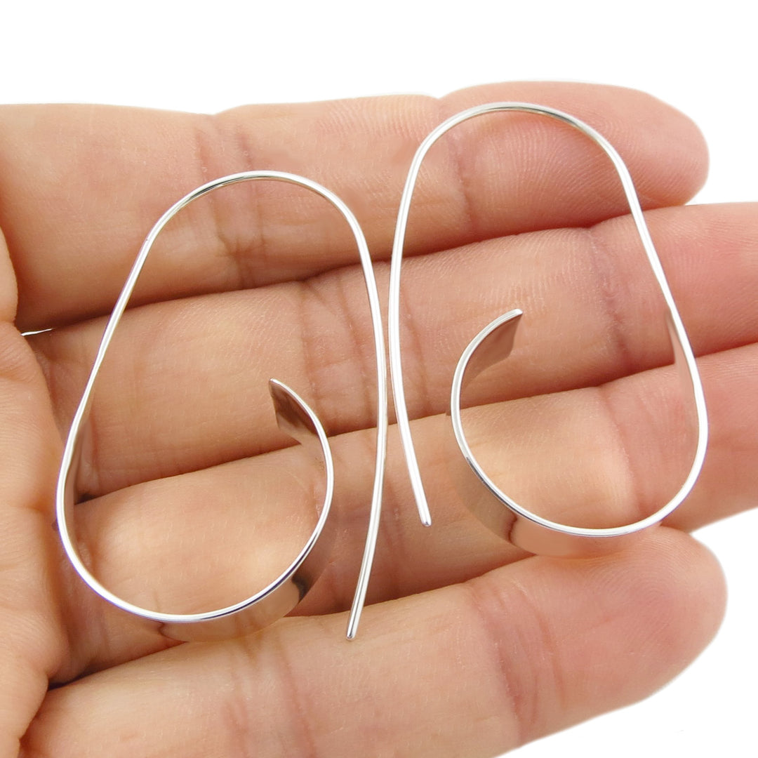 Silver hoop earrings held between fingers on a white background