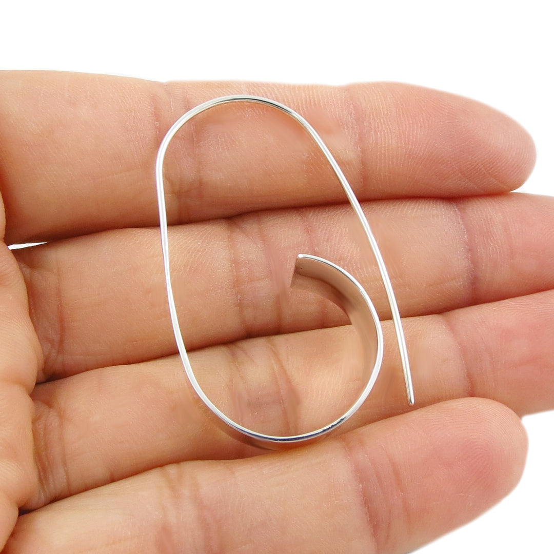 A single silver hoop earring held in a hand against a white background