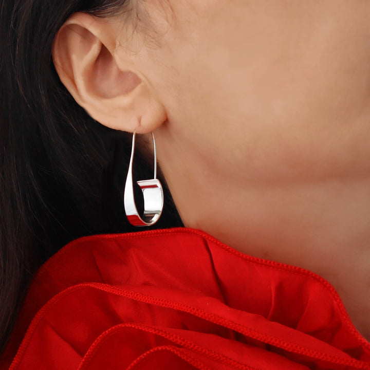 Long silver threader hoop earring worn by a woman with a red dress in the background