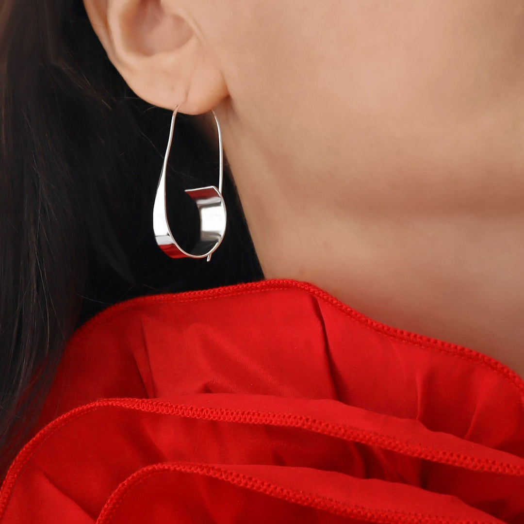 Large sterling silver hoop earring worn by a woman with a red garment in the background