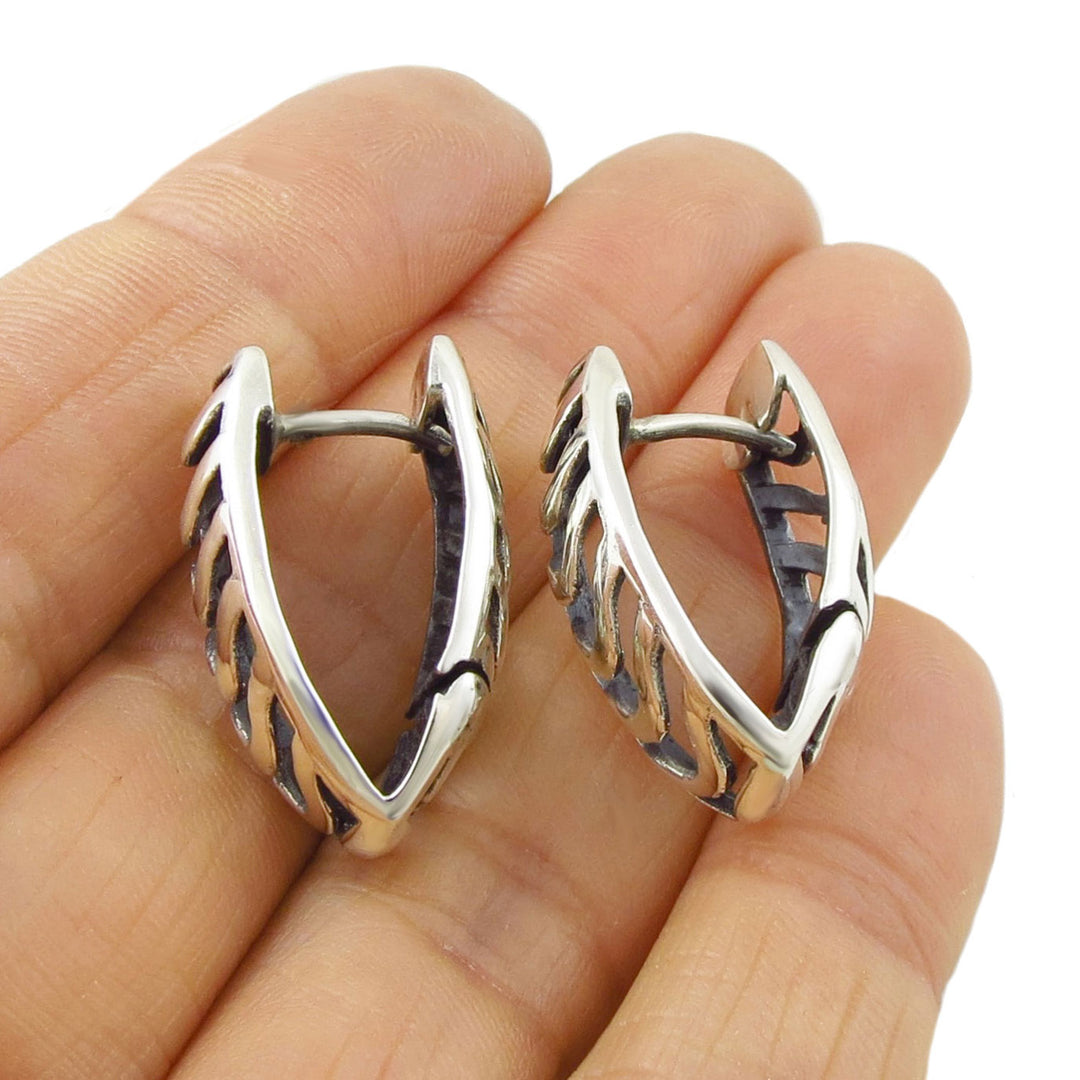 A pair of sterling silver huggie hoop earrings with a textured, leaf-like cutout pattern, shown resting on a woman's hand against a white background.