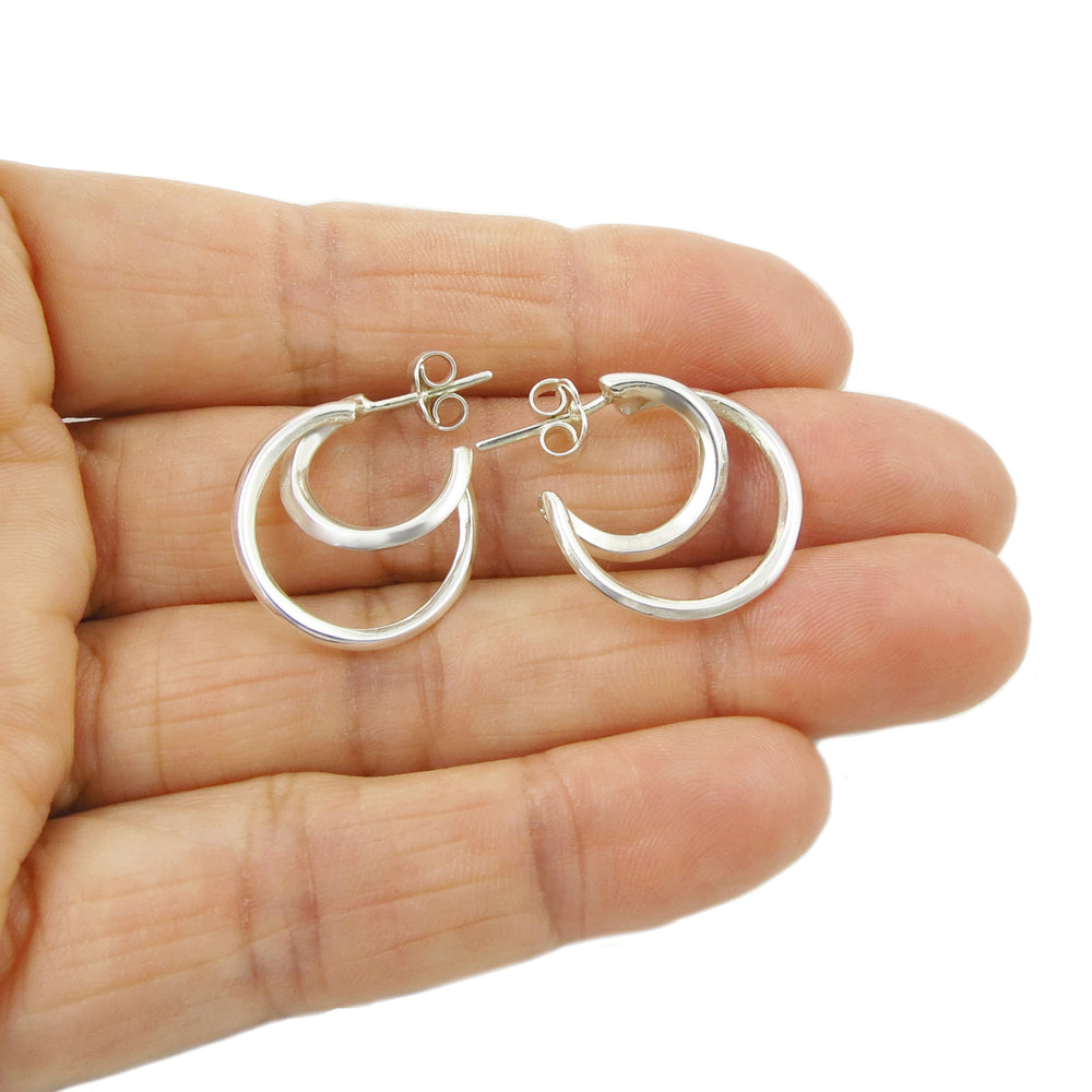 A pair of silver hoop earrings held in a hand, showcasing their double hoop design.