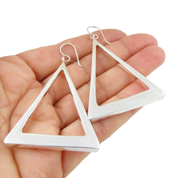 A pair of large Mexican sterling silver triangle hoop earrings held in a persons hand