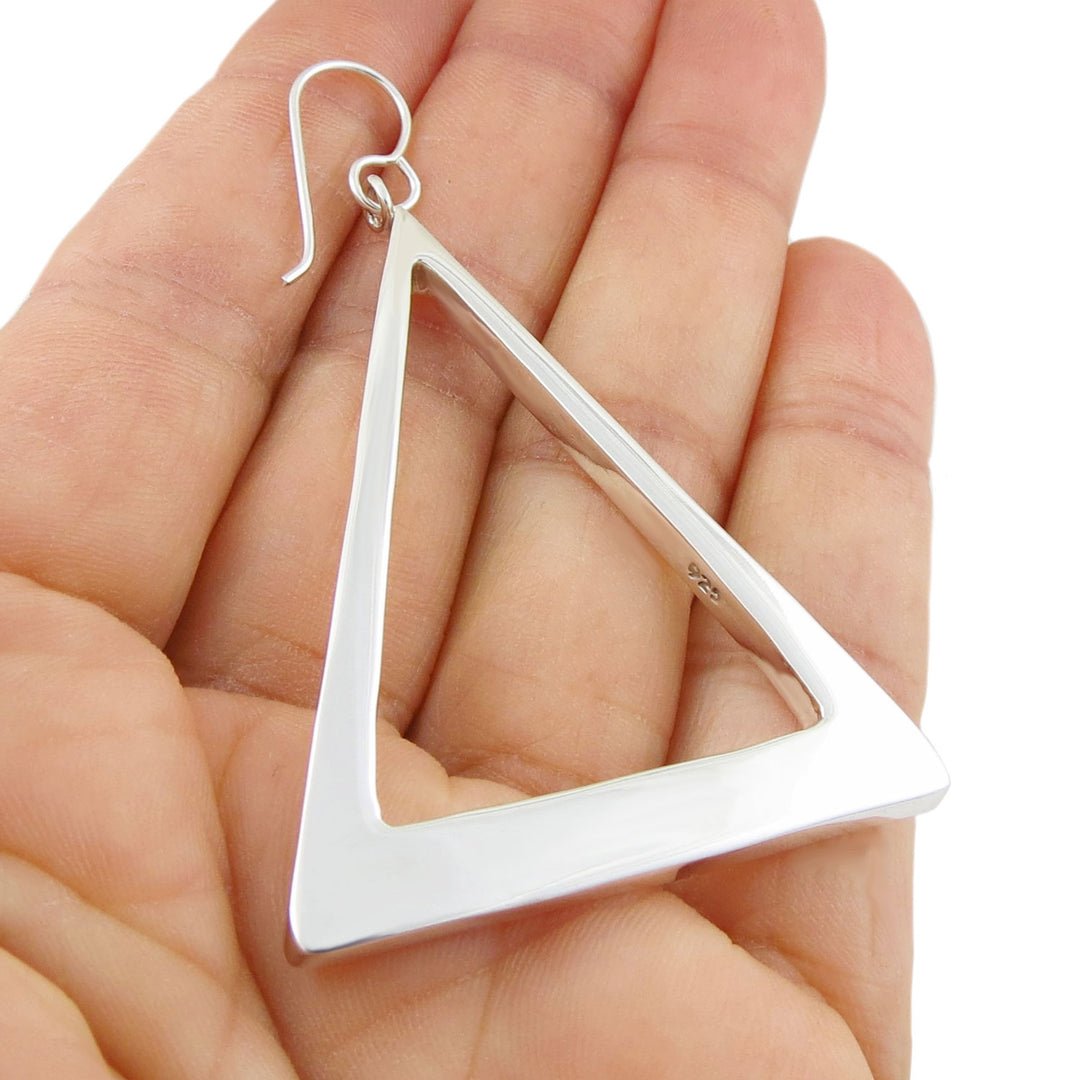 A single large angling triangle earring in 925 silver held in a persons hand. 