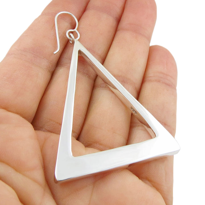 A single large angling triangle earring in 925 silver held in a persons hand. 