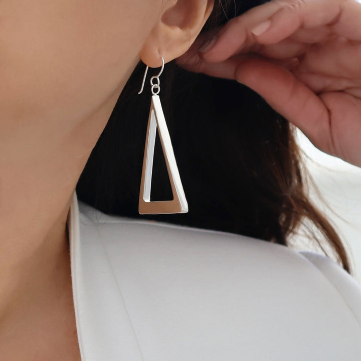 A large Taxco sterling 925 silver handmade geometric triangle dangling earring worn by a woman in a white jacket. 