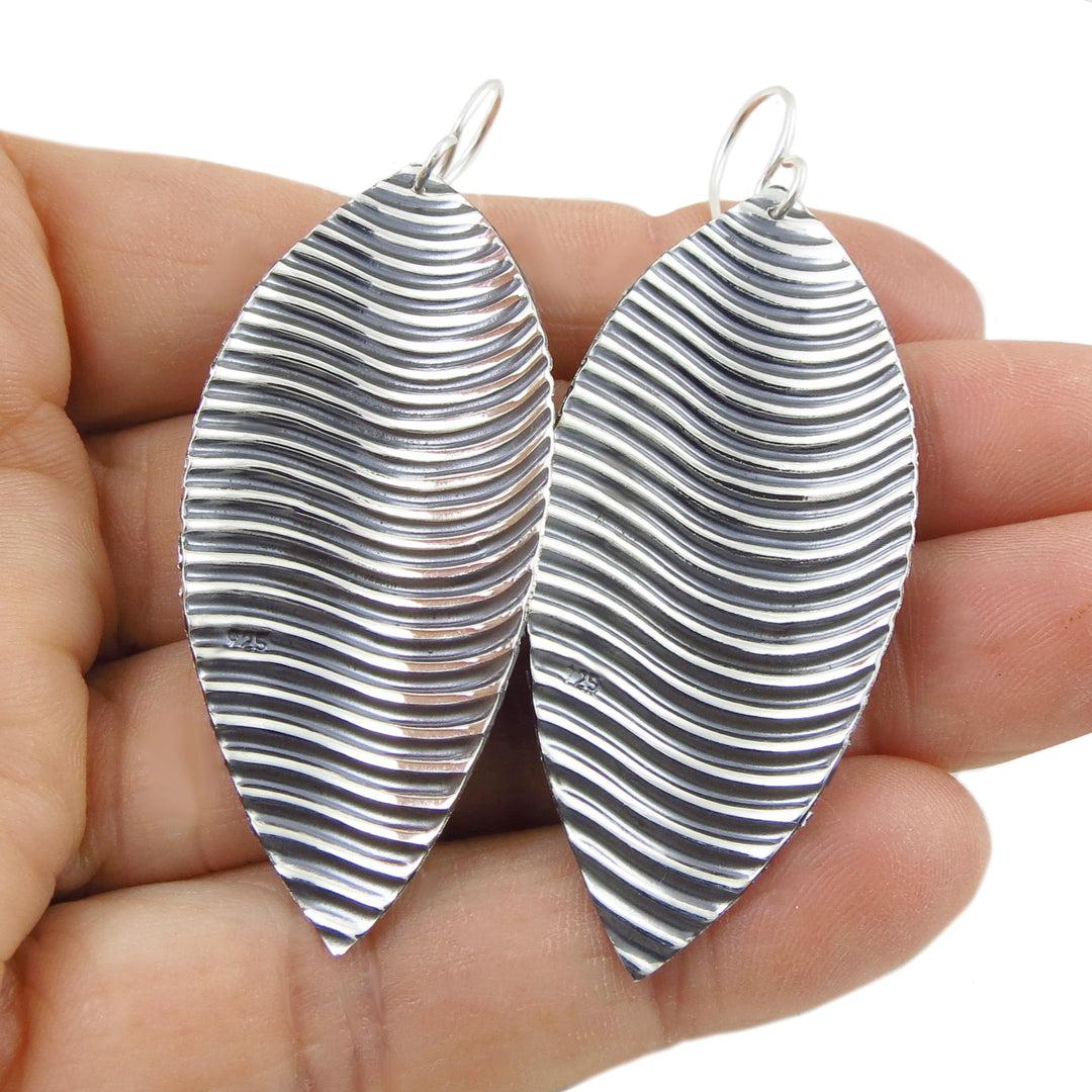 Silver and black striped 925 sterling silver handmade earrings held in a hand against a white background