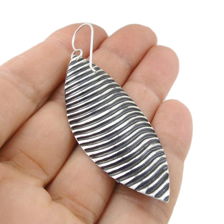 Hand holding a unique black and white striped large feather-shaped earring against a white background