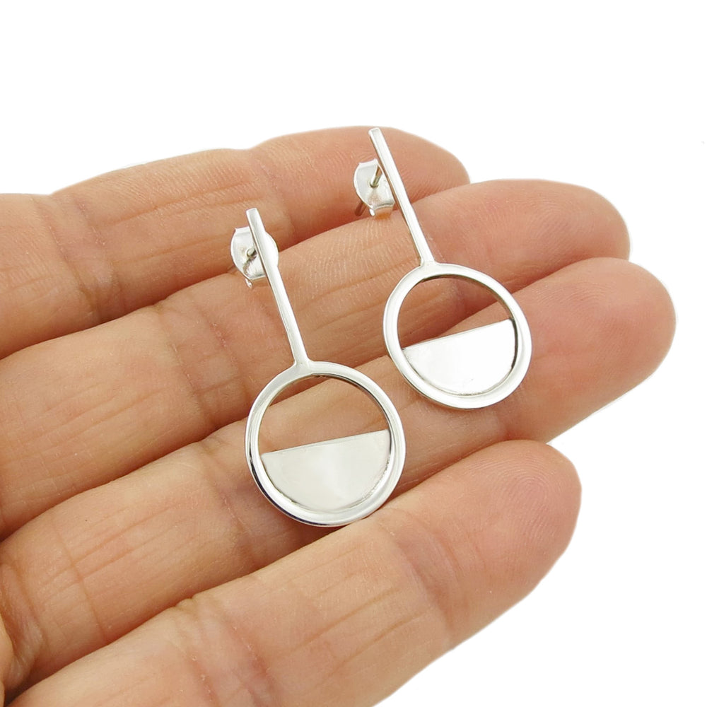 A pair of geometric sterling silver circle stick earrings being held in a person's hand.
