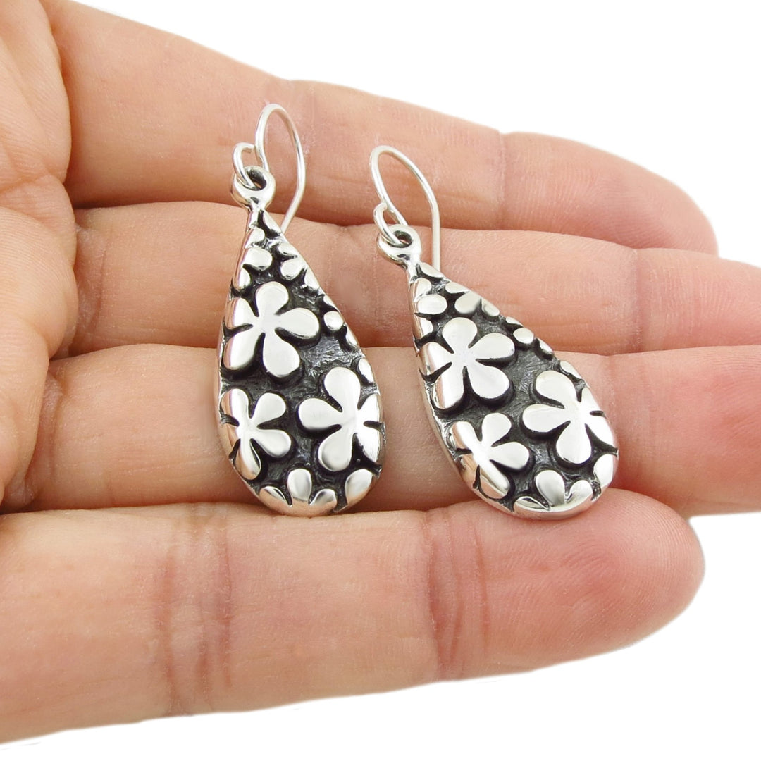 Handmade mexican 925 sterling Silver teardrop earrings with daisy flower patterns held in a hand against a white background