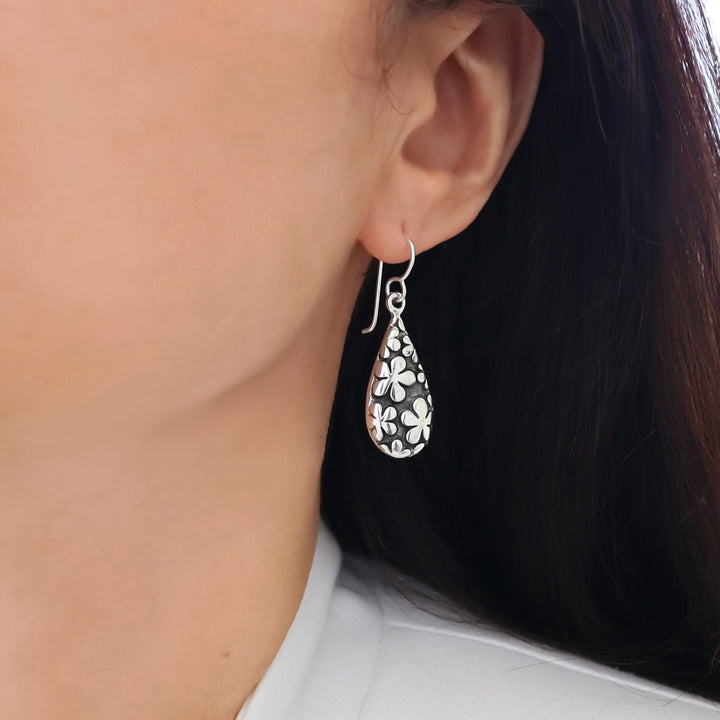 A woman with dark hair wearing a bold unique handmade 925 sterling silver terdrop earring decorated with polished daisy flowers. 