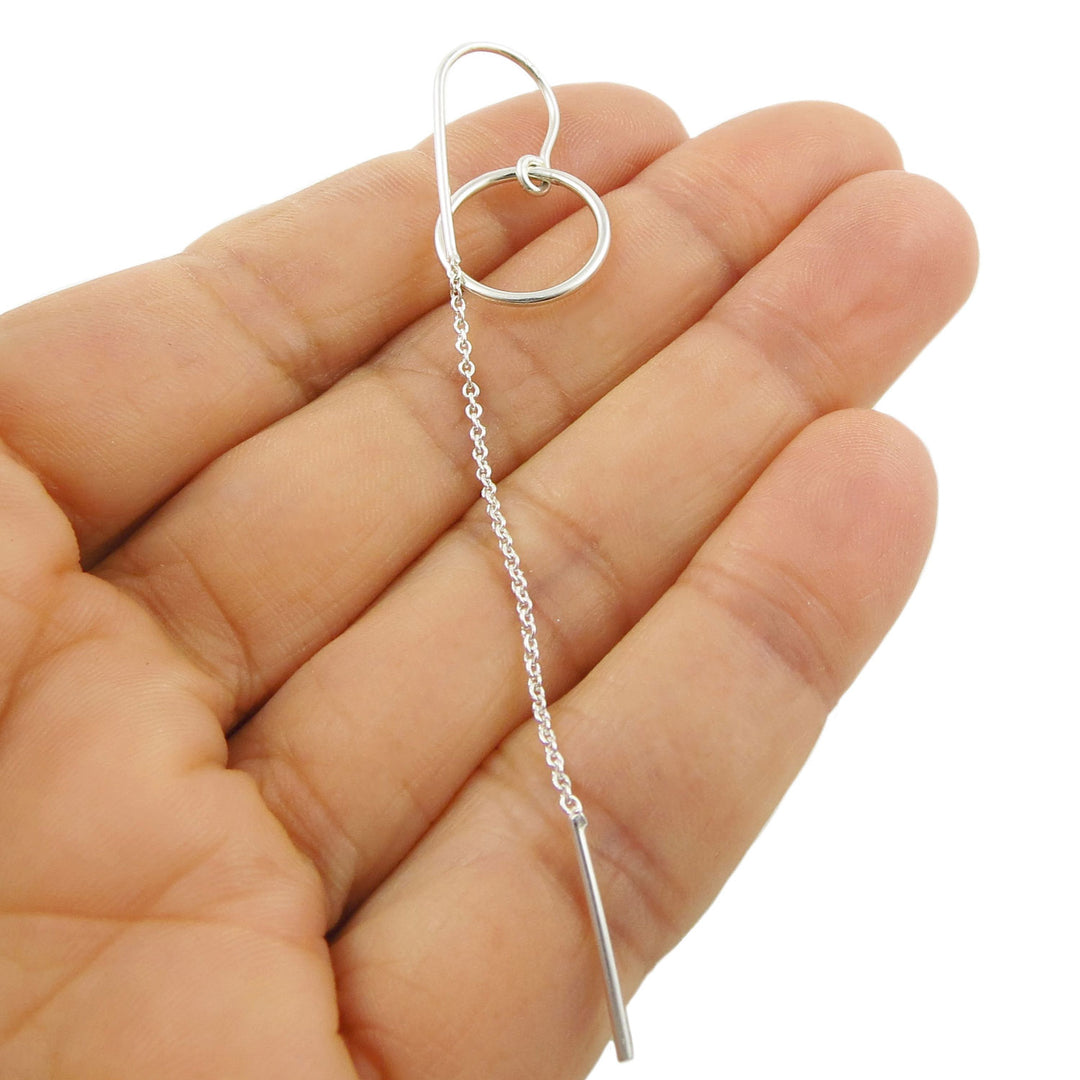 Sterling 925 silver lognm threader chain and circle earring held between fingers on a white background