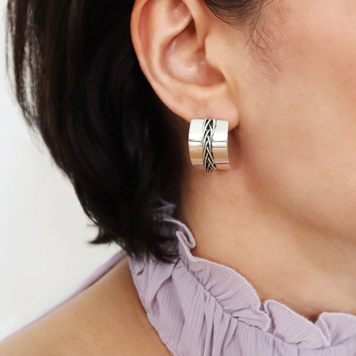 A large Mexican 925 sterling silver half hoop earring with a woven detail down the middle worn by a woman with dark hair and a purple top