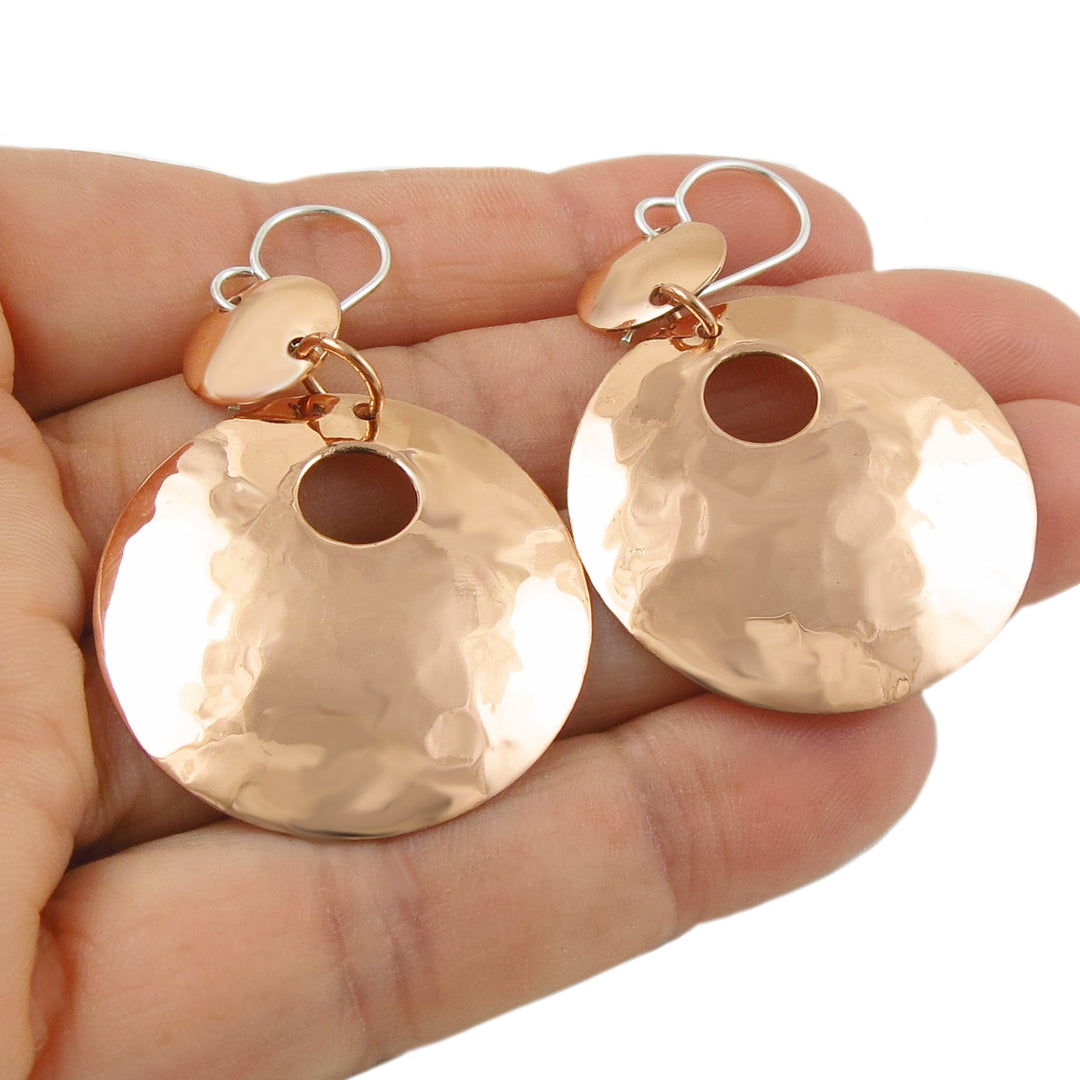 Large two tone daangling circle disc earrings in 925 silver and hammered copper held in a hand against a white background