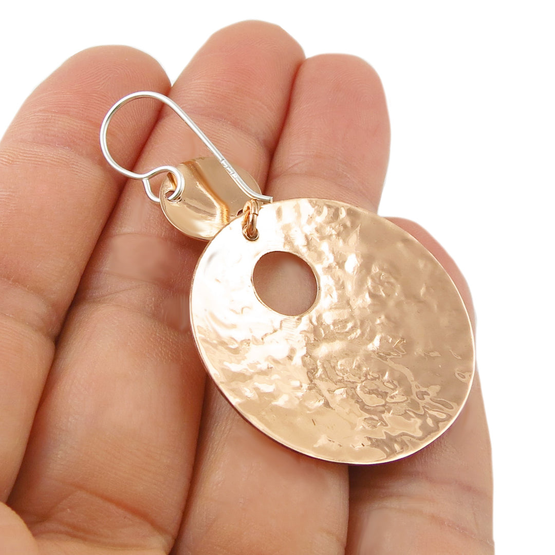 The underside of a round copper and 925 silver handmade two tone earring held in a hand against a white background