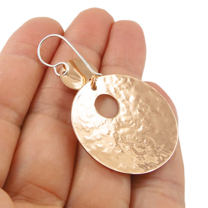 The underside of a round copper and 925 silver handmade two tone earring held in a hand against a white background